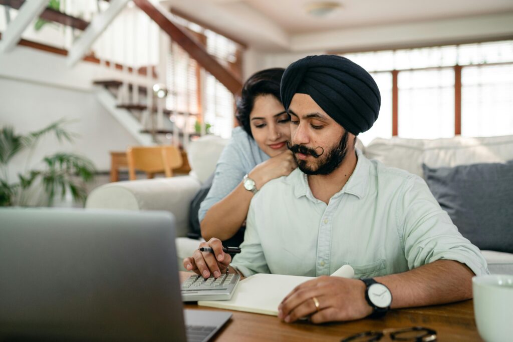 pexels-photo-4308058-4308058 Young smiling woman hugging concentrated husband from behind while counting bills on calculator in modern apartment